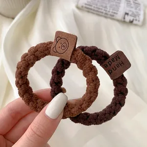 Close-up of two plush elastic hair ties in light and dark brown with leather labels
