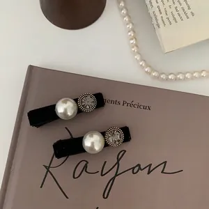 Elegant pair of black velvet hair clips with oversized pearls and rhinestones on a book