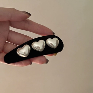 Retro black velvet hair clip with three silver heart studs shown in hand for women