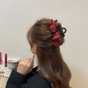 Detail view of large red tweed bow hair claw clip with golden threads on a model