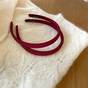 Close-up of handmade wine red satin headbands with black brand tags on white knitwear