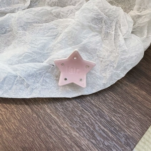 Dettaglio di un fermaglio a stella in acetato rosa con strass e incisione centrale