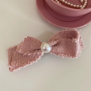 Detail of pink tweed bow hair clip with central pearl on a white surface