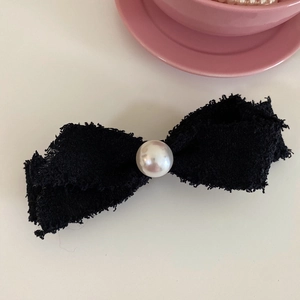 Detailed close-up of a black tweed bow hair clip featuring a white pearl embellishment