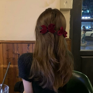 Detail view of burgundy velvet bow hair clips worn on brunette wavy hair in a cozy setting