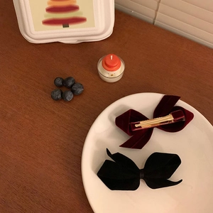 Elegant red and black velvet bow hair clips set on a decorative white ceramic tray