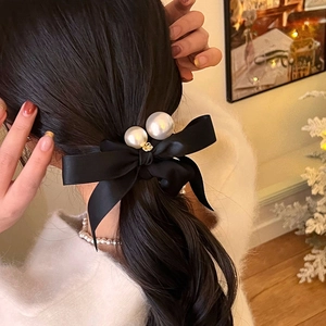 Detail of elegant black satin bow hair tie with dual pearls on a woman ponytail