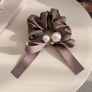 Elegant brown satin scrunchie with pearls and ribbon bow decoration on a table