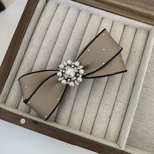 Elegant beige bow hair clip with black trim and pearl rhinestone center in jewelry box