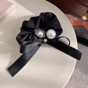 Detail of black satin scrunchie with white pearls, ribbon bow, and small metal logo charm
