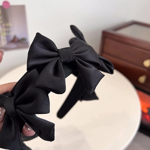 Gros plan d'un serre-tête en satin noir avec nœuds montrant la texture soyeuse et élégante