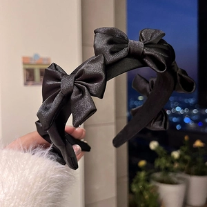 Détail d'un serre-tête en satin noir montrant la texture et les nœuds élégants