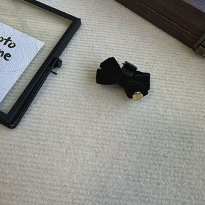 Detail of a black velvet bow hair clip with a gold metal emblem on a beige background