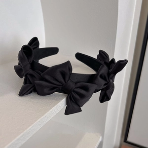 Serre-tête élégant en satin noir avec nœuds 3D multiples sur un socle blanc minimaliste