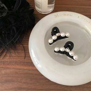 Elegant pair of black mini hair claws with white pearls and clear crystals in a dish