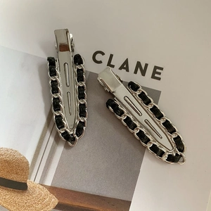 Detail showing two silver metal chain hair clips with black weave on a magazine