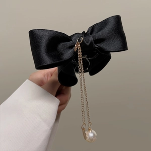 Close-up of black satin bow hair clip with gold metal chains and elegant white pearl detail