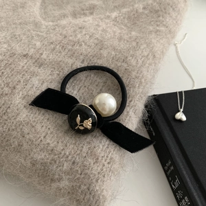 Dettaglio dell'elastico per capelli con fiocco di velluto nero, perla bianca e rosa incisa
