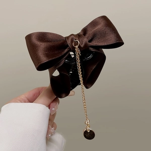 Detail of elegant dark coffee satin bow hair claw clip with golden chain and round pendant