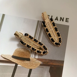 Set of two gold metal hair clips with black leather chain detail on a magazine
