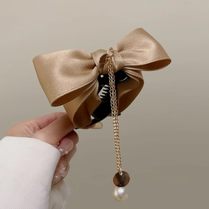 Detail view of champagne gold satin bow hair claw with a dangling pearl pendant