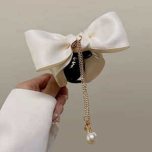 Detail of cream satin bow hair claw clip with golden chain tassel and pearl pendant