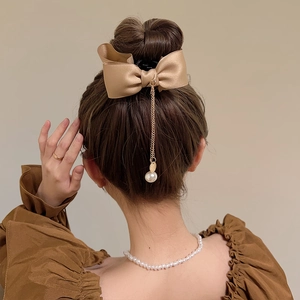 Detail of champagne satin bow hair claw with gold chain tassels and a large pearl pendant