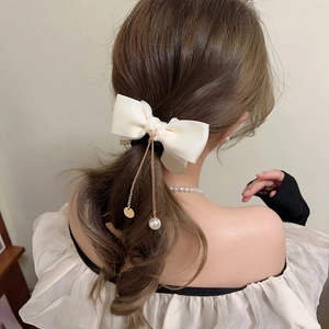 Elegant cream silk bow hair claw with gold chain tassels and pearls on model hair