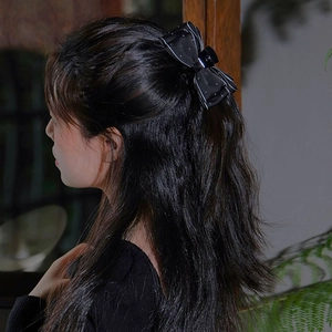 Detail of a black polka dot silk bow hair claw clip styled on a semi-tied hairstyle