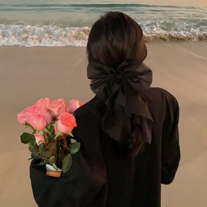 Barrette élégante avec grand nœud en organza noir pour femme sur une plage au coucher du soleil