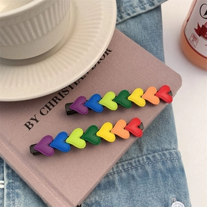 Close-up of two rainbow heart hair clips with gradient colors on black metal pins