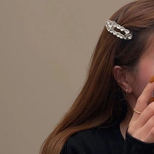 Détail d'une barrette ovale en cristal et de bagues dorées sur un mannequin
