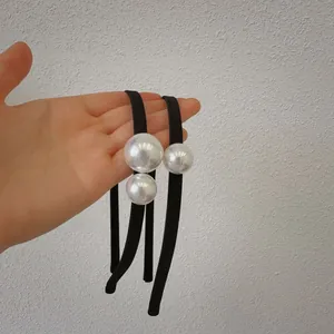 Close-up of thin black headbands featuring glossy large white pearls and fabric texture