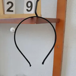 Detail of minimalist black headband featuring a single large white pearl ornament on a thin band