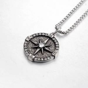 Macro detail of silver compass pendant necklace with sparkling crystal and North East South West engraving