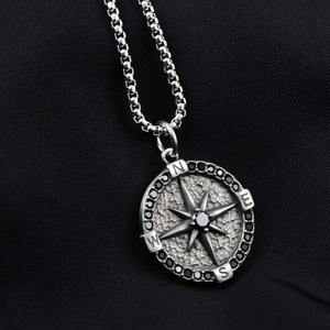 Close-up of compass pendant necklace with black rhinestones on dark fabric background