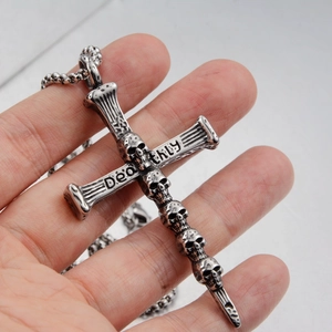 Gros plan d'un pendentif croix gothique en acier inoxydable avec crânes et texte Deathly