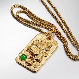 Goldene Tiger-Halskette mit grünem Edelstein auf gebürsteter Metalloberfläche