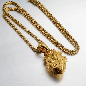 Detail eines anatomischen Herzanhängers in Gold mit dicker Kugelkette auf Metallfläche