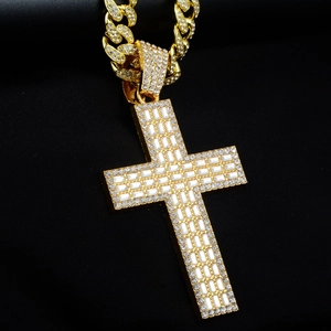 Détail macro du pendentif croix dorée avec zircons rectangulaires et chaîne gourmette cubaine