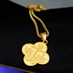 Détail d'un pendentif religieux doré avec relief en croix et bordure florale sur chaîne
