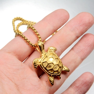 Detailed close-up of a gold-plated turtle pendant necklace held by hand showing turtle texture