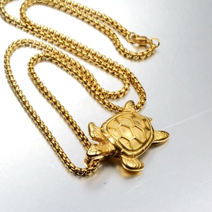 Detailed close-up of a golden turtle pendant with a polished shell and sleek ball chain