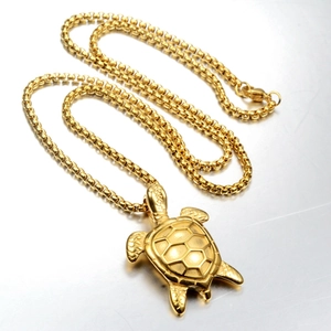 Detailed view of a golden turtle pendant with box chain on a brushed metal surface