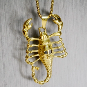 Close-up of golden scorpion pendant necklace with skull detail on a wooden backdrop