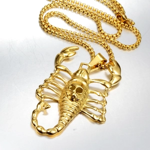 Detailed close-up of golden scorpion pendant with skull motif on heavy curb chain