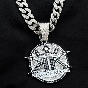 Macro detail of iced-out silver pendant with King of Kings text and thick cuban link