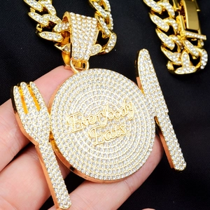 Gros plan du pendentif doré avec couverts et gravure Everybody Eats sur la plaque