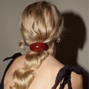 Close-up of a high-gloss dark red U-shaped resin hair tie on a blonde ponytail