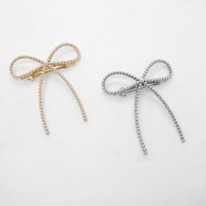 Détail de barrettes nœuds avec perles blanches et pompons en métal doré et argenté